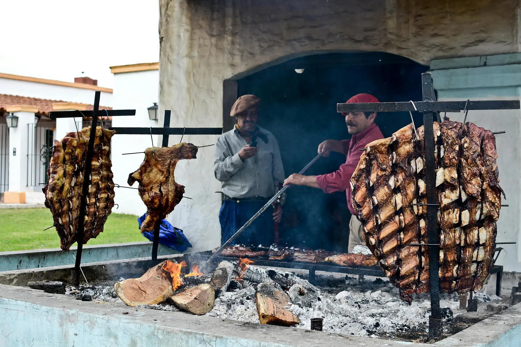 Whole lamb splayed on a metal cross roasting over a wood fire.
