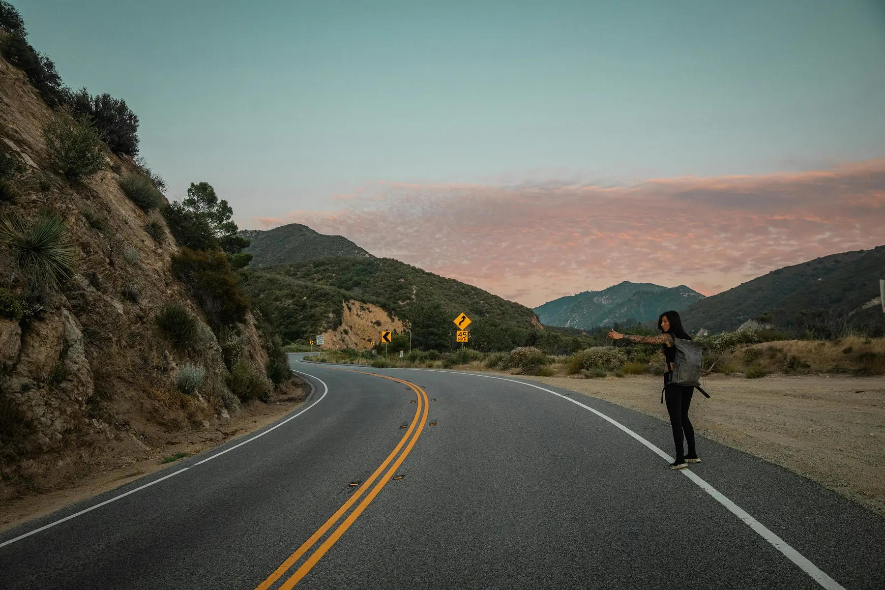 A traveler with a cardboard sign waiting at a Patagonian road junction.